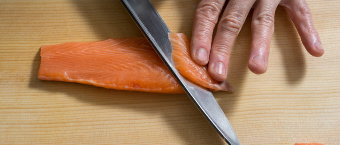 Cutting raw salmon with a knife on cutting board