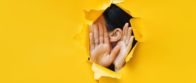 Ear and hands poking through yellow paper