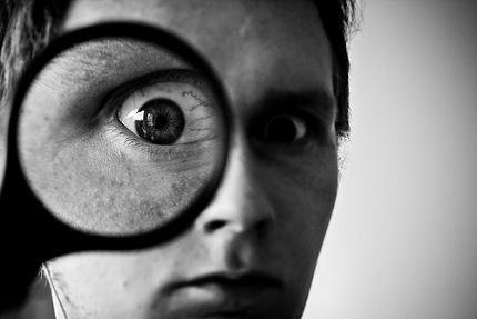 Man holding up magnifying glass, making one eye look much bigger than the other.