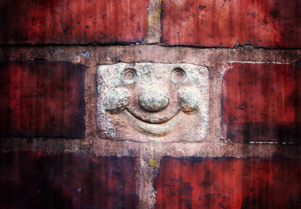 Brick wall with a funny face sculpted on one brick
